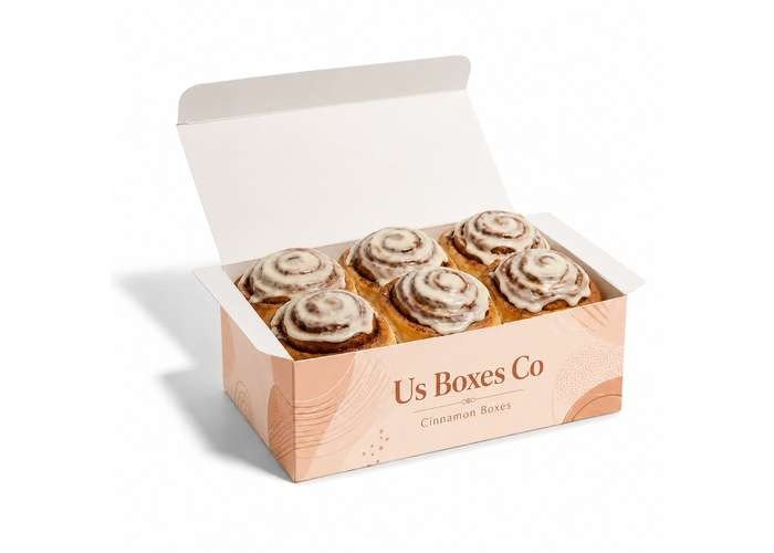 Open peach-colored bakery box containing six iced cinnamon rolls.